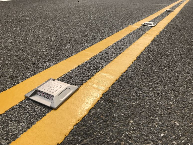 Image shows recently painted road lane markings with reflector in the forground